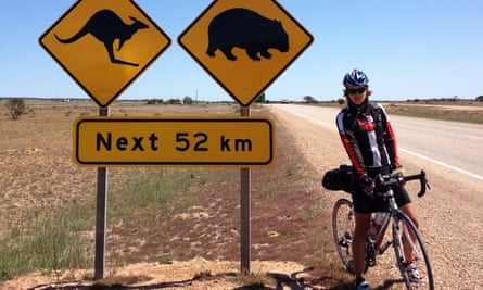 Juliana Buhring standing astride her bike on an empty road next to animal warning roadsigns.