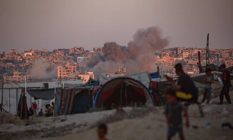 Smoke rises following an Israeli air strike as internally displaced Palestinians sit next to their tents in Khan Younis camp, southern Gaza Strip, 13 August 2024.