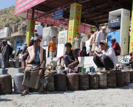 People sit and crouch on a line of gas cylinders outside a gas station