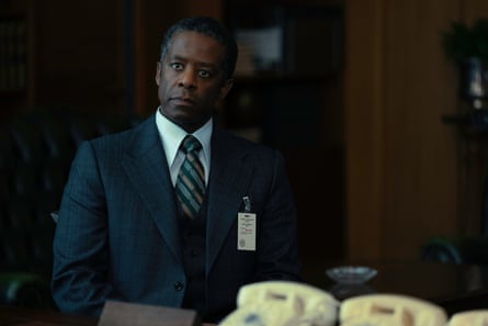 A man in a suit stands behind a row of phones.