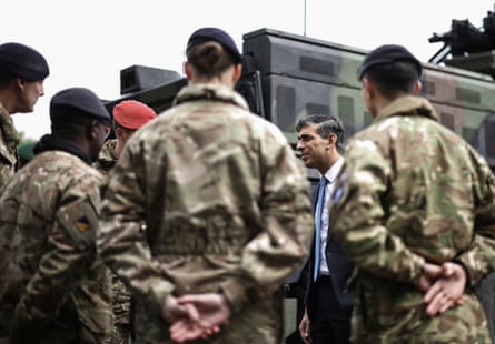 sunak, in suit, speaks with people wearing military fatigues