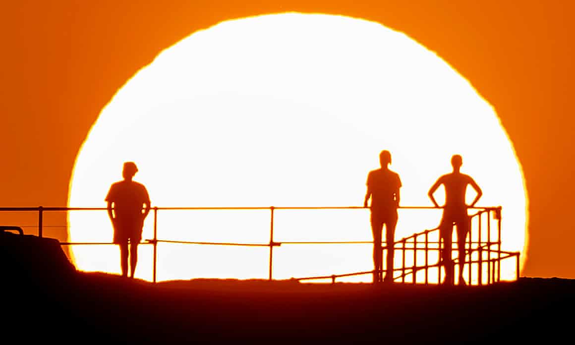 People standing on a platform, silhouetted by a big, low sun