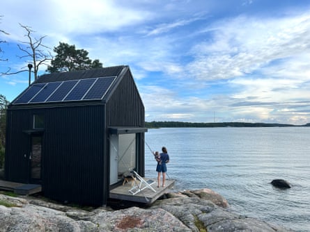 A small black cabin with solar panels on rocks right next to the sea