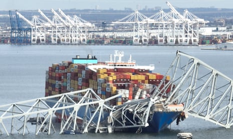 a large ship with many brightly colored metal containers and mangled white metal pieces of a bridge in a body of water