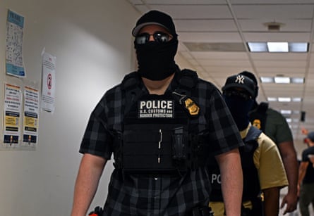a man in a corridor wearing a mask and sunglasses and a police vest