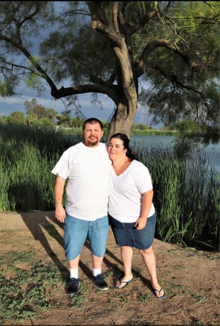 couple stands in front of tree and lake with arms around each other