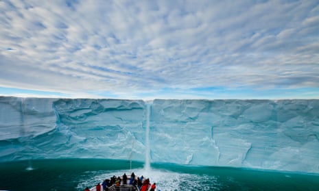 Under a blanket of clouds, tourists watch a meltwater waterfall on an icecap.