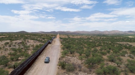 Aerial view of a car driving on a dirt road in a scrubby desert landscape.
