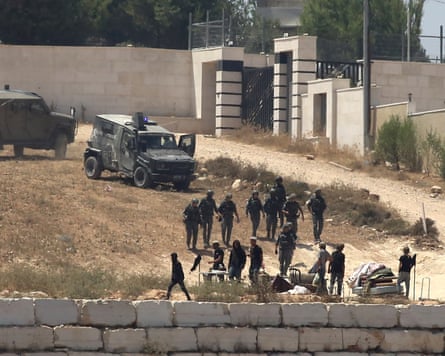 Israeli soldiers stand guard next to settlers in front of Palestinian homes that they have blockaded in the village of Qusra.