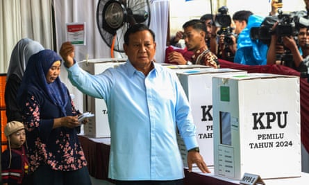 Prabowo Subianto standing by a ballot box, holding up his ballot paper