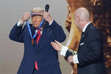 Donald Trump puts on the inaugural Fifa peace prize presented to him by Gianni Infantino during the 2026 World Cup draw.