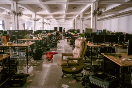 A very large abandoned office with banks of desks with computer screens and paper and other debris scattered around