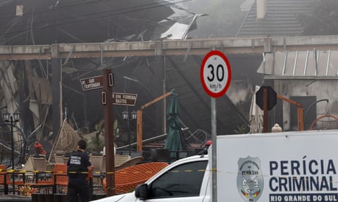 A Brazilian police van is parked alongside the smoke-wreathed wreckage of a building that was hit by the plane