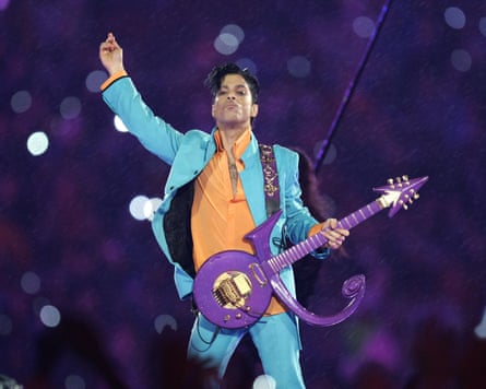 Prince on stage in turquoise suit, orange shirt and purple guitar.