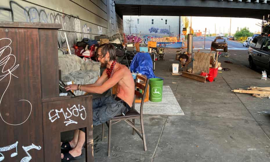 Tyson Morlock plays piano next to a swimming pool hooked to a fire hydrant under a freeway underpass during a heatwave in Portland, Oregon.