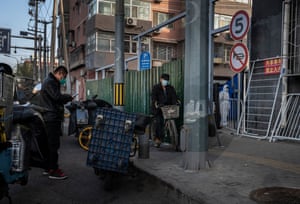 A delivery driver waits near a barricade in a community under lockdown as an epidemic control worker stands guard in Beijing, China