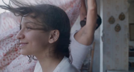 A still from Nezouh, with a young girl, her hair blowing in the wind, and a man behind her in a vest trying to hang a curtain or some fabric.
