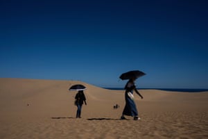 Tourists holding parasols walk through sand dunes