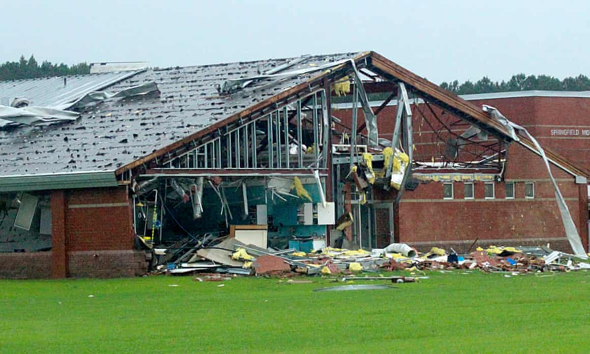 A storm-damaged middle school with some walls missing is seen standing amid debris on a green lawn.