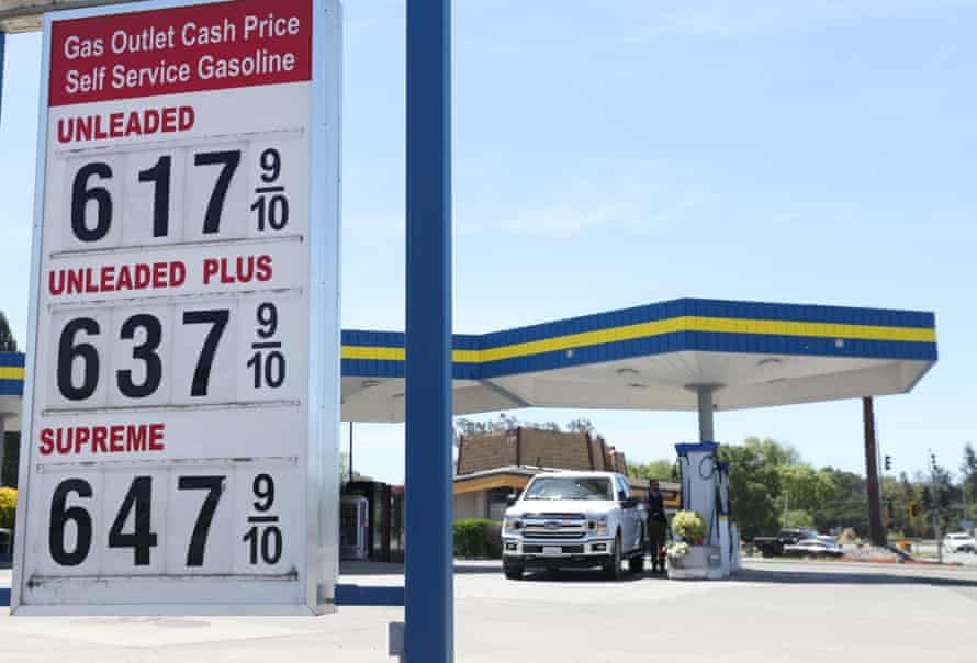 Un panneau devant une station-service affiche des prix pour un gallon d'essence allant de 6,17 $ à 6,47 $.  En arrière-plan, un homme remplit le réservoir de son gros camion blanc.