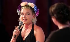 Florence Pugh in flowery headdress and black halter- neck holds a mic