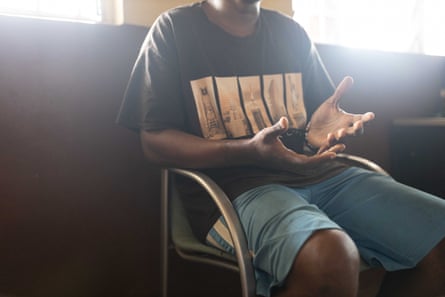 Ahmed sits in a chair wearing black T-shirt and green shorts.