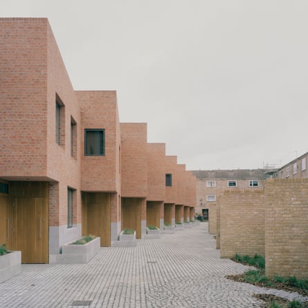 A row of redbrick homes with wooden doors, facing diagonally out onto a paved walkway