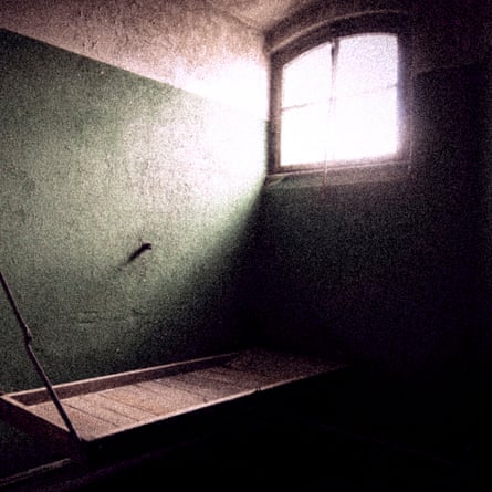 A prison cell with a wooden bench for a bed, bare walls and a small window
