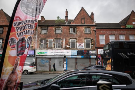 A view across a road of shop fronts sealed by metal shutters covered in graffiti