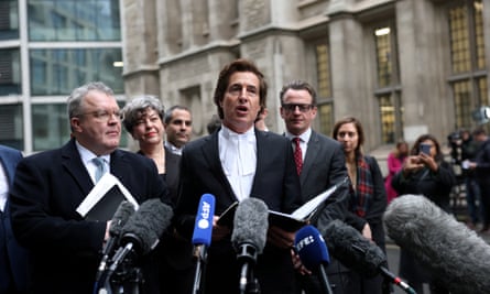 Lawyer talks to assembled journalists with microphones pointed towards him and crows around