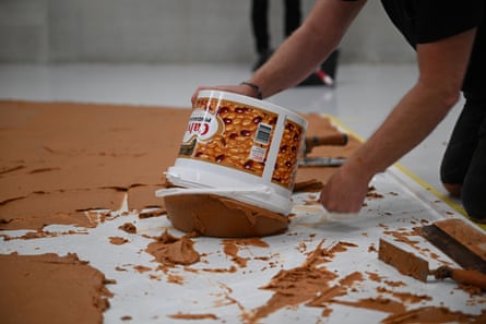 A man tips out a very large tub of peanut butter onto the floor
