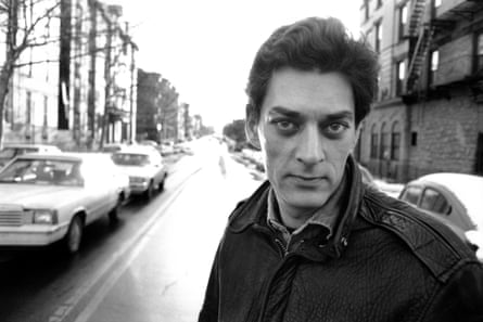 Black and white photo of Paul Auster on a residential street lined with cars