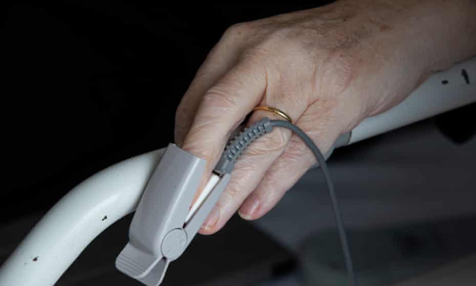 A woman's hands on a hospital bed wearing a pulse oximeter