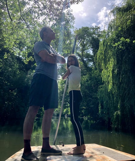 Paul Laity and his daughter Martha Mills standing on a boat in a river, Martha holding a punting pole, surrounded by trees and sunshine