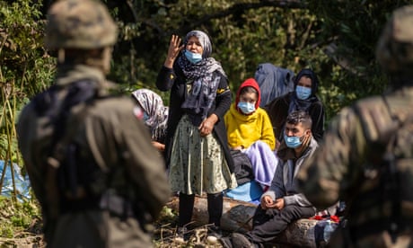 A woman talks to a Polish border guard as migrants believed to be from Afghanistan sit on the ground in the small village of Usnarz Górny near Białystok, northeastern Poland, located close to the border with Belarus, on August 20, 2021. - The fate of a group of 32 bedraggled migrants stranded at a makeshift encampment on the border between Belarus and Poland for nearly two weeks has sparked a heated debate in Poland.
