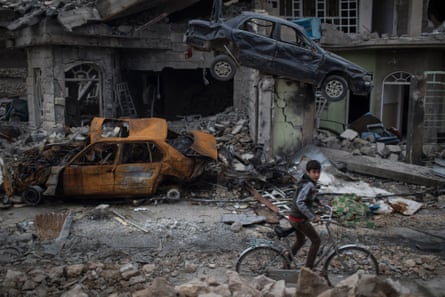 A boy rides his bike past destroyed cars and houses in a neighbourhood recently liberated by Iraqi security forces on the western side of the city, 19 March