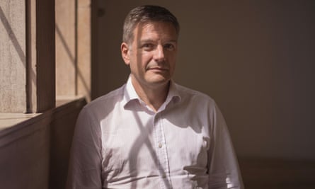 home visit policy nhs Brian Bell, in a cotton shirt slightly wrinkled towards the waist, stands near a sunny window, smiling