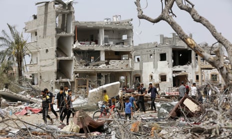 people walk along a road surrounded by rubble and destroyed buildings