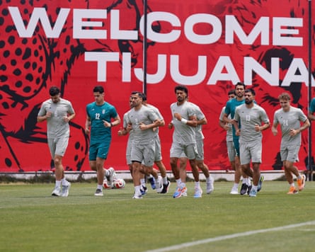 Players jogging on pitch under red Welcome sign