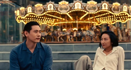A man and a woman sit in front of a fairground carousel