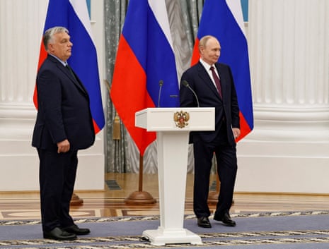 Orban and Putin stand in front of a line of Russian flags.