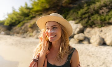 Young woman applying sunscreen at the beach<br>Photo of a young woman applying sunscreen on her face
