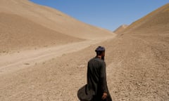 A man in a turban walks in a barren desert-like landscape