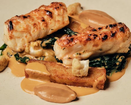 Two pieces of roasted monkfish served on cavolo nero and thick pieces of fried potato surrounded by a beige sauce.