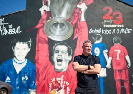 Jamie Carragher standing with his arms folded in front of a giant mural featuring Carragher hoisting the European Cup in 2005, adorns the gable end of a neighbouring building. Christopher Thomond for The Guardian.
