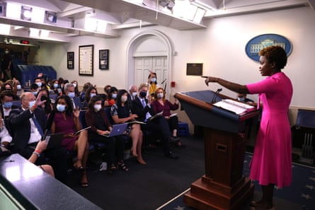 A woman in a pink dress points to a person in the crowd seated before her.