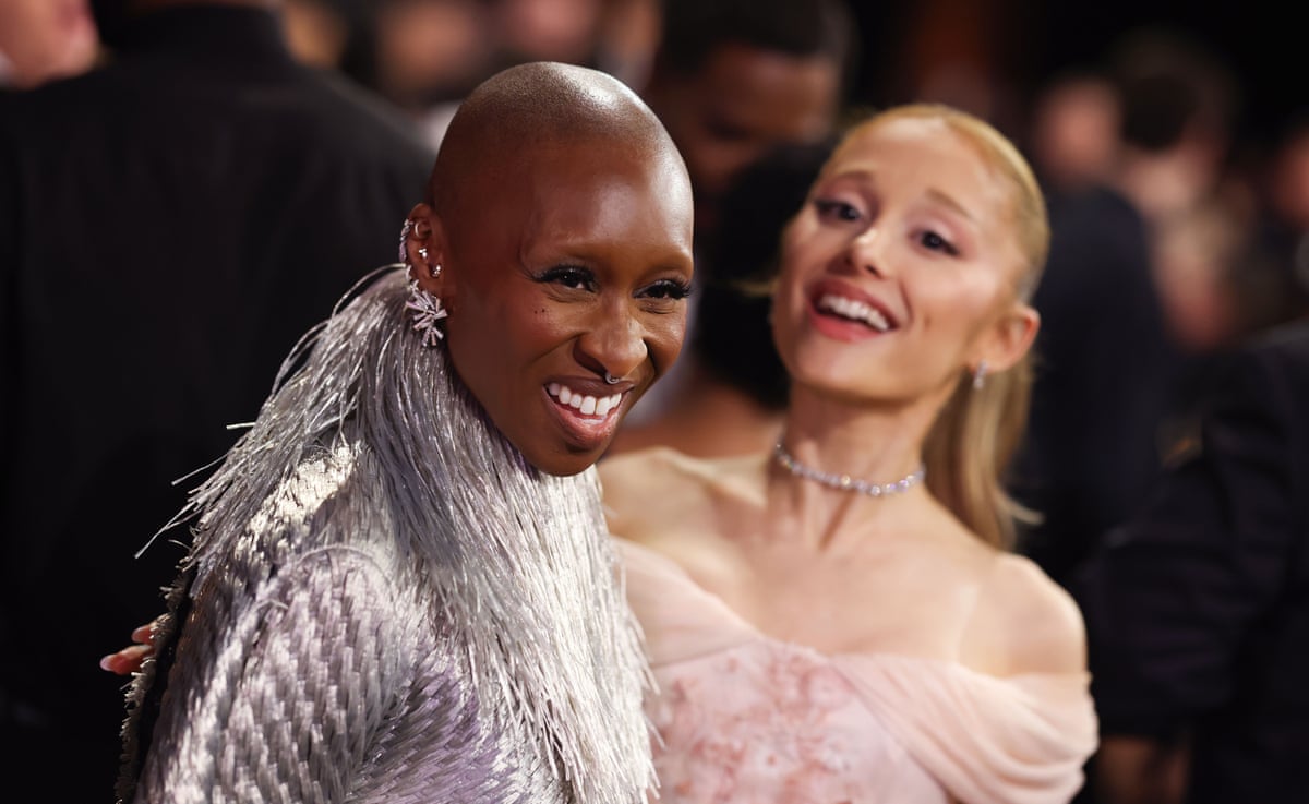 Cynthia Erivo and Ariana Grande smiling and wearing evening dresses