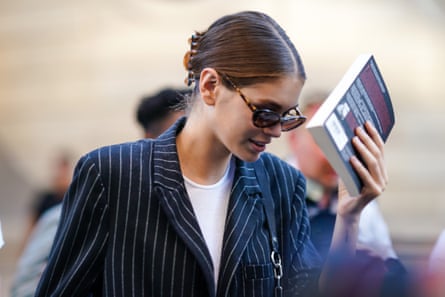 Kaia Gerber hides her face behind a book in front of photographers, outside Valentino, during Paris Fashion Week