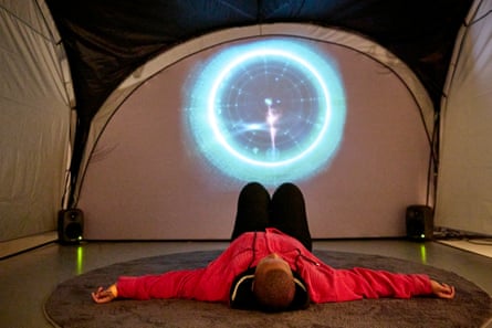 a person lies on their back in a tent, with some kind of astrology chart projected on to the far side of the tent