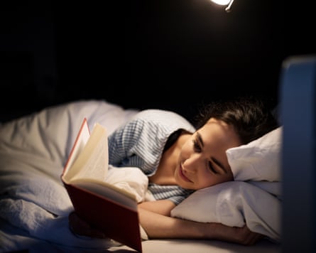 Young woman lying in her bed reading a book at night
